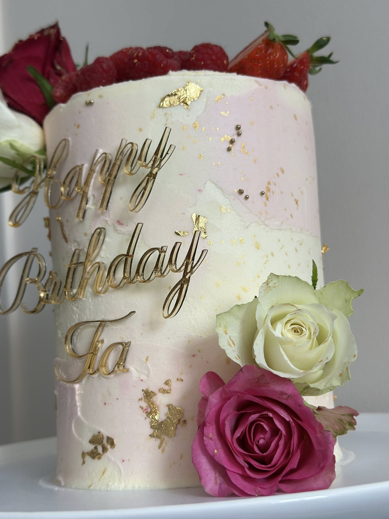 Elegant two-tier birthday cake with gold leaf and fresh flowers