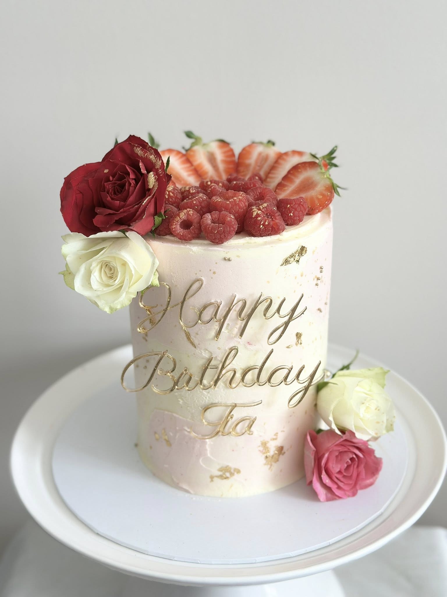 Elegant birthday cake with roses, berries, and gold lettering