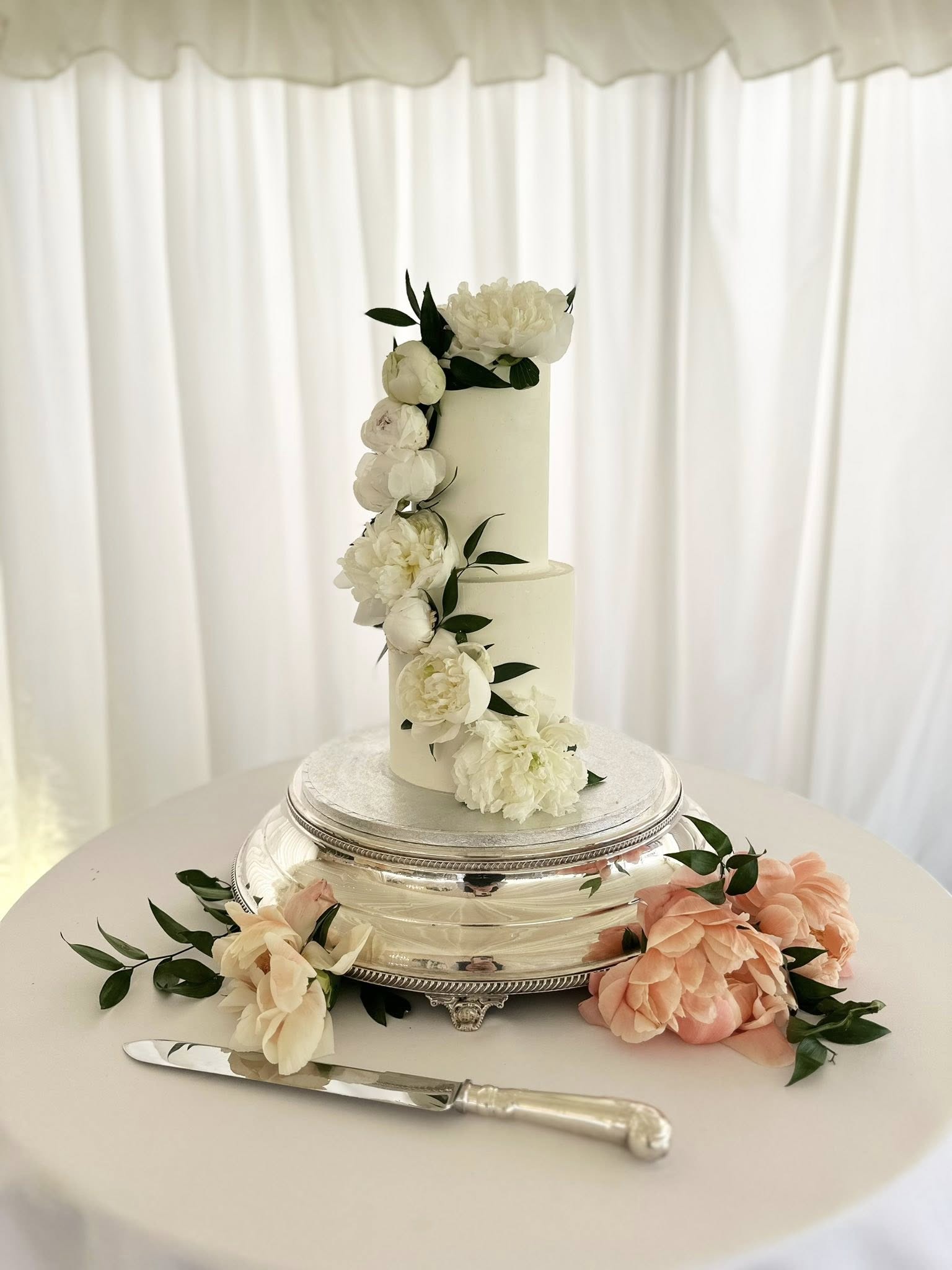 Elegant two-tier wedding cake with white peonies and pink flowers